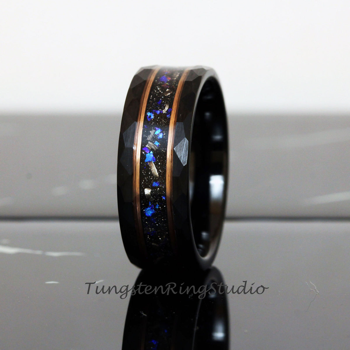 May include: A black tungsten carbide ring with a hammered finish and a copper inlay. The inlay is filled with blue and silver glitter.
