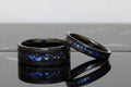May include: Two black tungsten carbide rings with a blue and purple glitter inlay. The rings have a beveled edge and a brushed finish.
