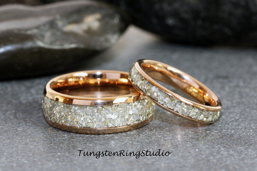 May include: Two rose gold tungsten carbide wedding bands with a row of small, clear, faceted stones set into the band.