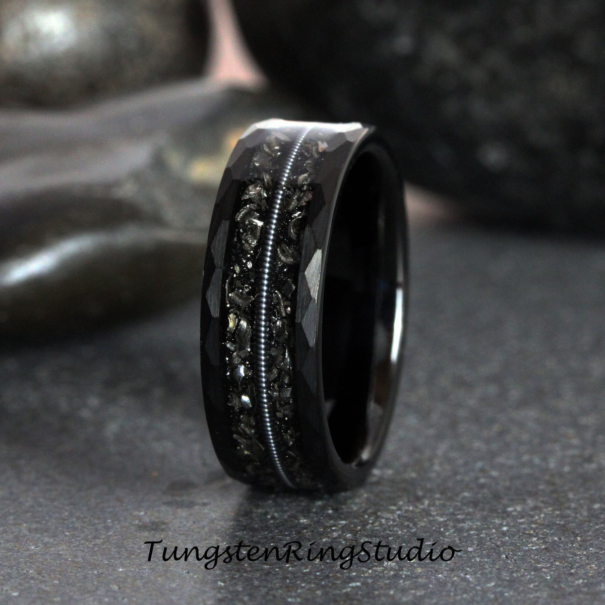 May include: A black tungsten carbide ring with a hammered finish and a thin silver line down the center. The ring has a textured, almost rough, surface.