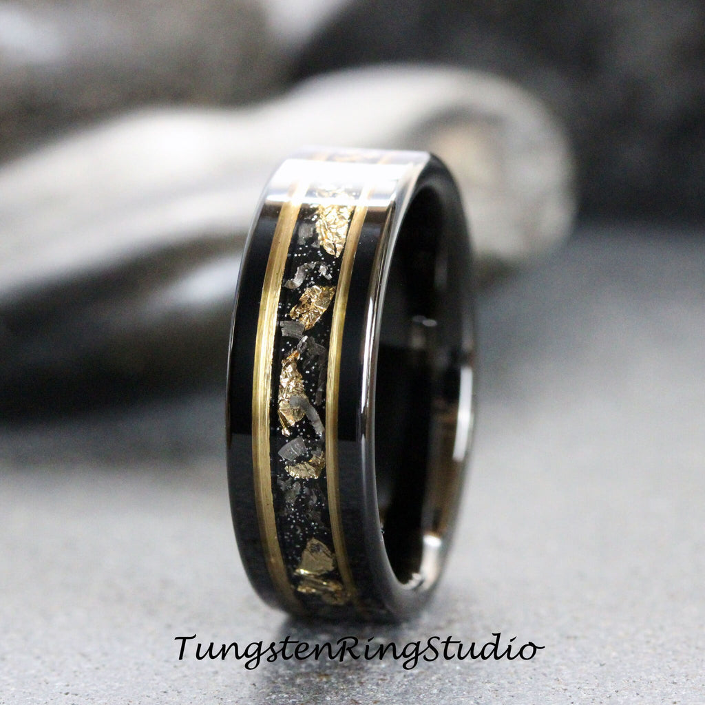 May include: A black tungsten carbide ring with a gold inlay and black and gold flecks. The ring has a polished finish.