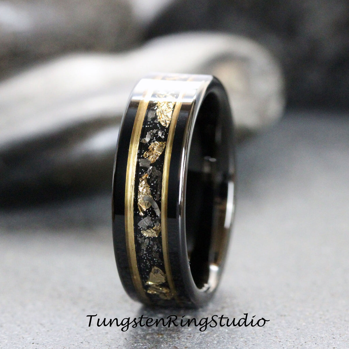May include: A black tungsten carbide ring with a gold inlay and black and gold flecks. The ring has a polished finish.