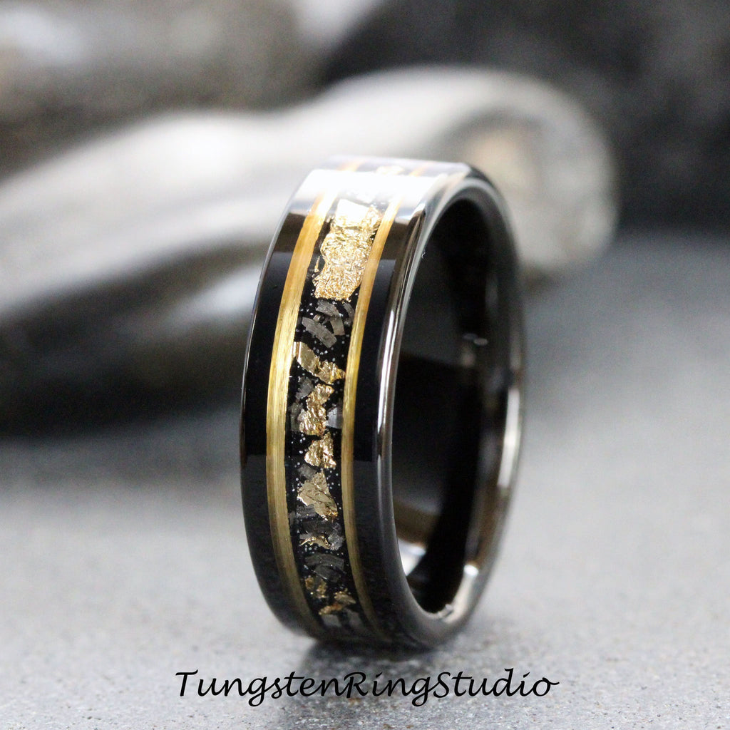 May include: A black tungsten carbide ring with a gold inlay featuring a scattered pattern of gold flakes. The ring has a polished finish.