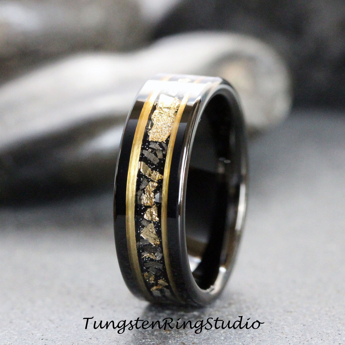 May include: A black tungsten carbide ring with a gold inlay featuring a scattered pattern of gold flakes. The ring has a polished finish.