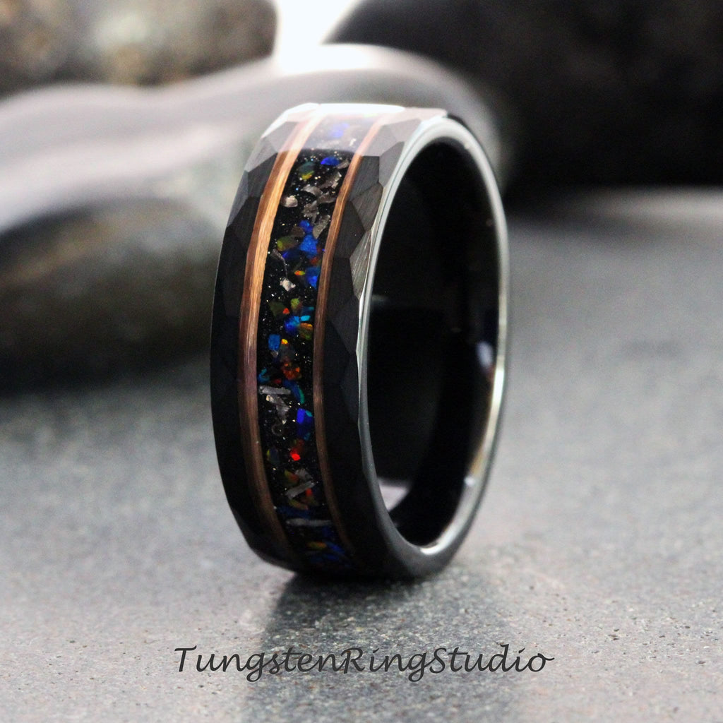 May include: A black tungsten ring with a faceted exterior and a central inlay of colorful, sparkling material. The inlay is framed by copper-colored metal bands. The ring is displayed on a gray surface. The text "TungstenRingStudio" is at the bottom.