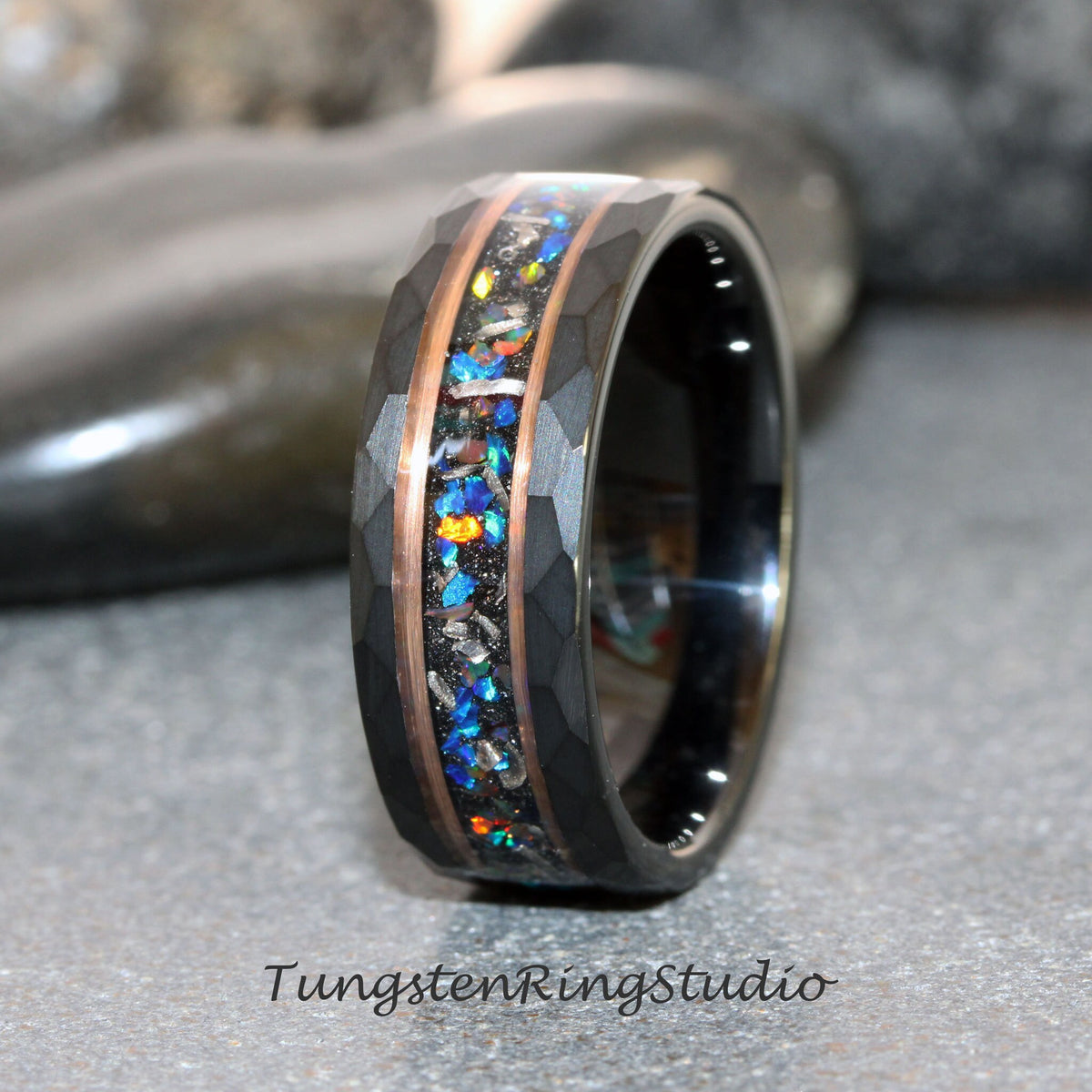 May include: Black tungsten ring with a hammered finish and a central inlay of colorful opal and copper accents. The ring features the text "TungstenRingStudio" at the bottom.