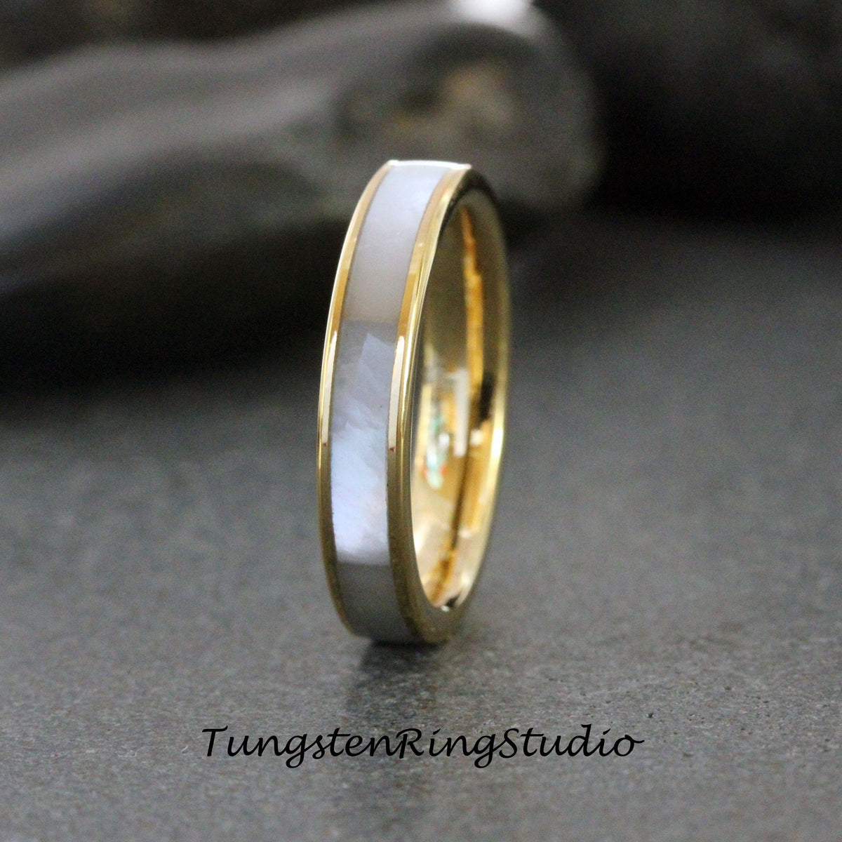 May include: A silver and gold wedding band with a white inlay. The band is polished and has a smooth finish.