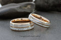 May include: Two matching tungsten carbide wedding bands with a rose gold inlay and a white inlay. The bands have a meteorite pattern.
