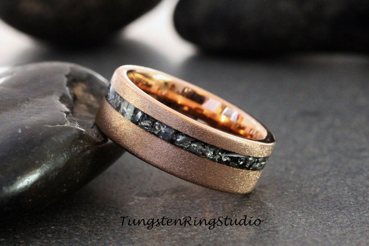May include: A rose gold tungsten carbide ring with a black meteorite inlay. The ring has a brushed finish and is set against a dark background.