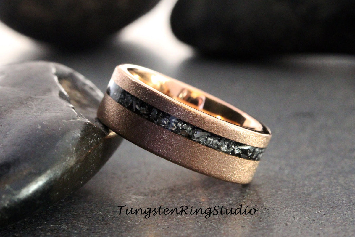 May include: A rose gold tungsten carbide ring with a black meteorite inlay. The ring has a brushed finish and is set against a gray background.