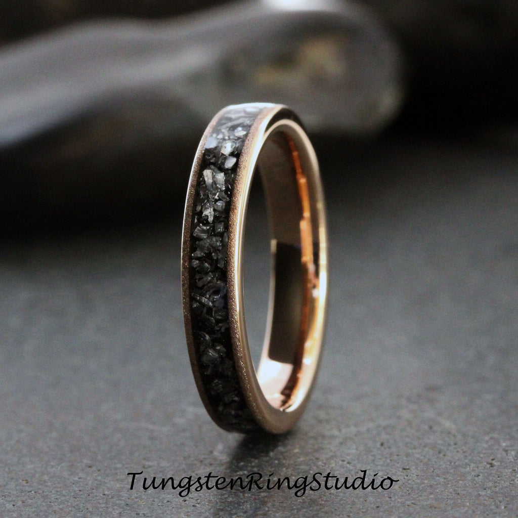 May include: A rose gold tungsten carbide ring with a black diamond inlay. The ring is a simple band with a smooth finish.