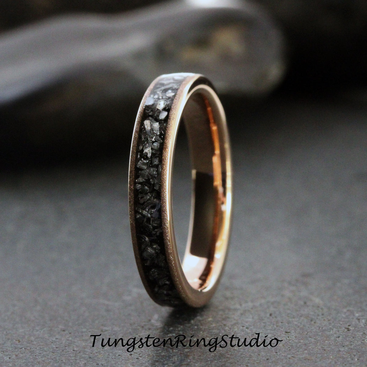 May include: A rose gold tungsten carbide ring with a black diamond inlay. The ring is a simple band with a smooth finish.