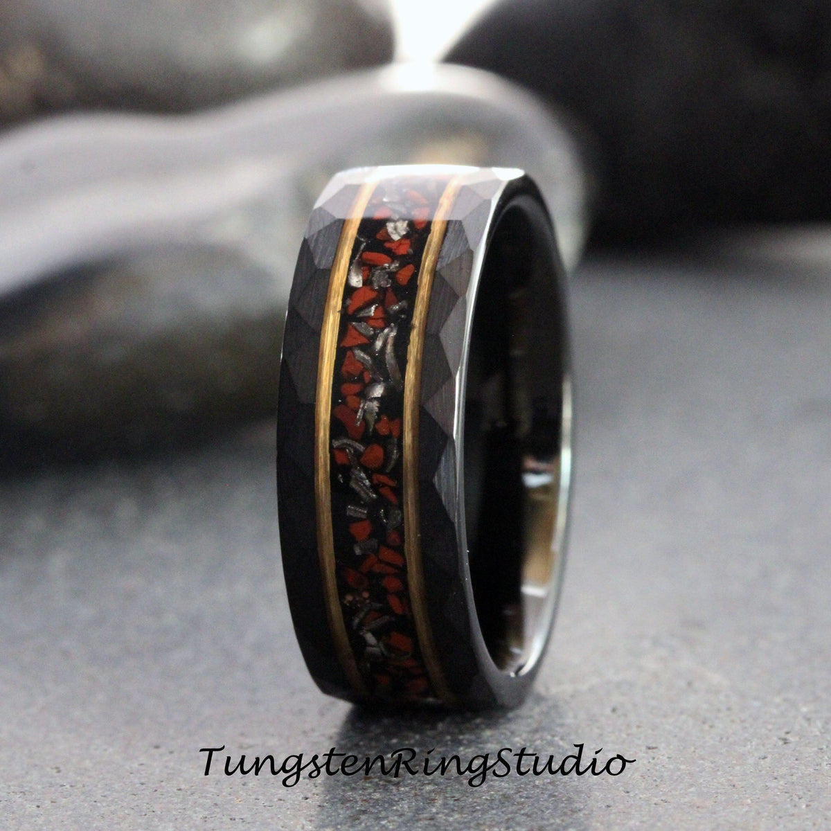 May include: A black tungsten ring with a red and gold inlay. The ring has a beveled edge and a hammered finish.