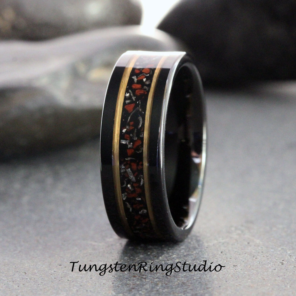 May include: A black tungsten carbide ring with a gold inlay and red and black speckled inlay. The ring is a wedding band.