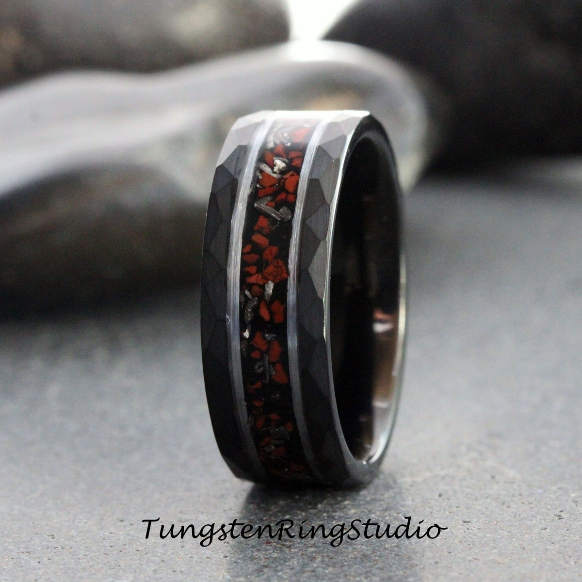 May include: A black tungsten carbide ring with a hammered finish and a red and silver inlay. The ring is approximately 8mm wide.