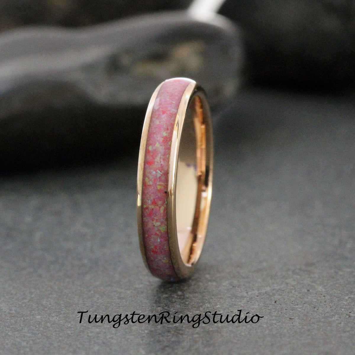 May include: A rose gold tungsten carbide ring with a pink opal inlay. The ring is a simple band with a thin inlay of pink opal.
