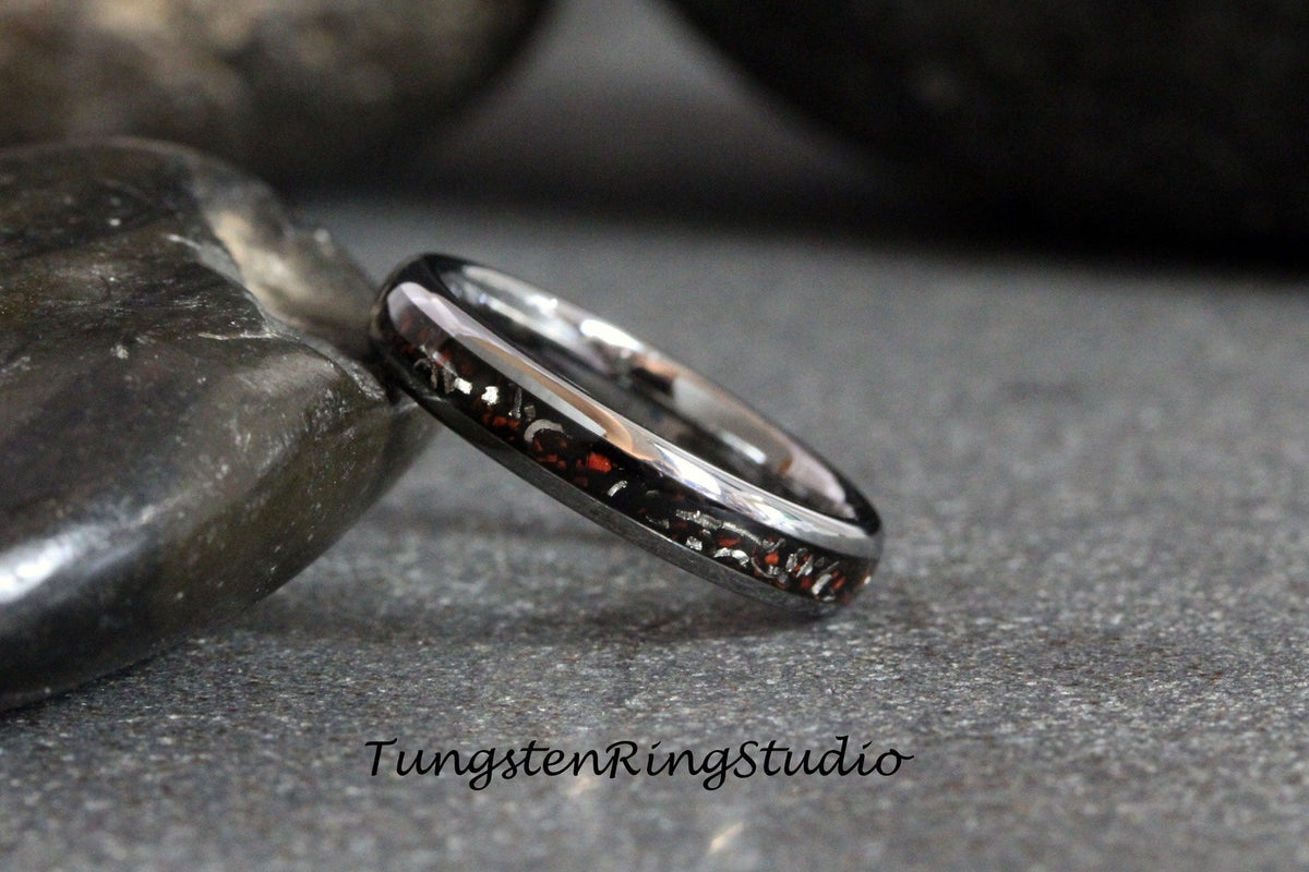 May include: A silver tungsten ring with a red and black inlay. The ring is polished and has a beveled edge.