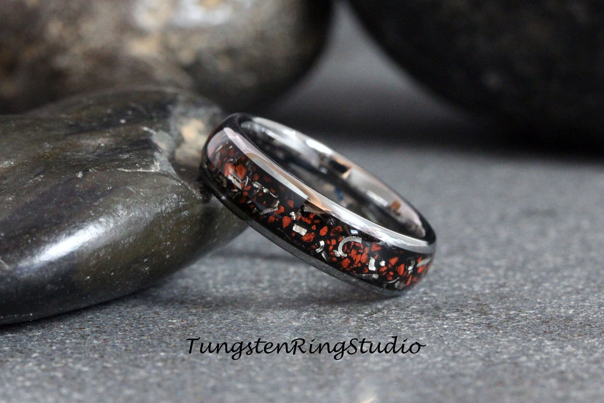 May include: A black tungsten ring with a red and silver inlay. The ring is on a gray surface.