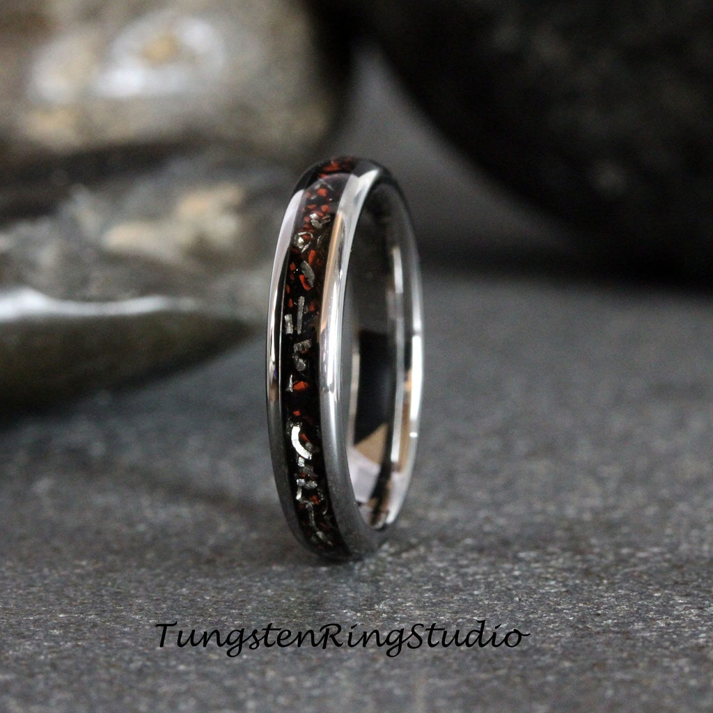 May include: A silver tungsten carbide ring with a black and red inlay. The inlay has a pattern of small, red and silver flecks.
