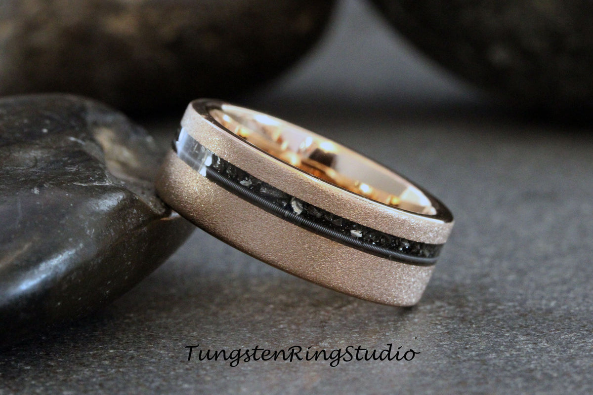 May include: A brushed rose gold tungsten carbide ring with a black inlay and black meteorite particles. The ring has a satin finish.