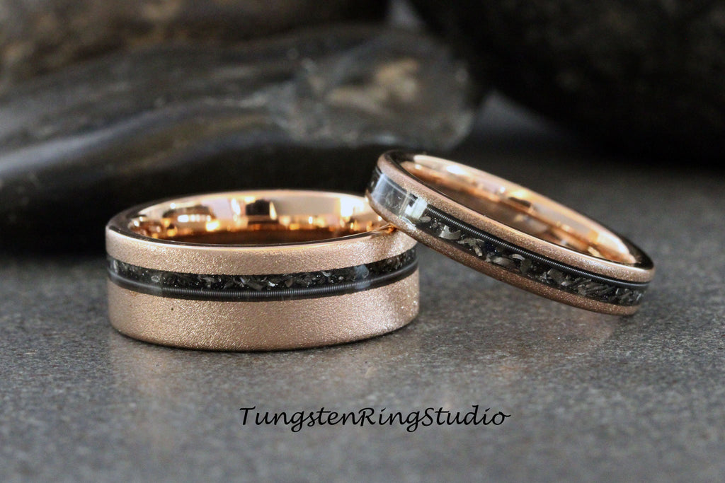 May include: Two rose gold tungsten carbide wedding bands with a black inlay. The bands have a brushed finish and a thin black line with black specks.