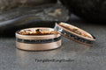 May include: Two rose gold tungsten carbide wedding bands with a black inlay. The bands have a brushed finish and a thin black line with black specks.