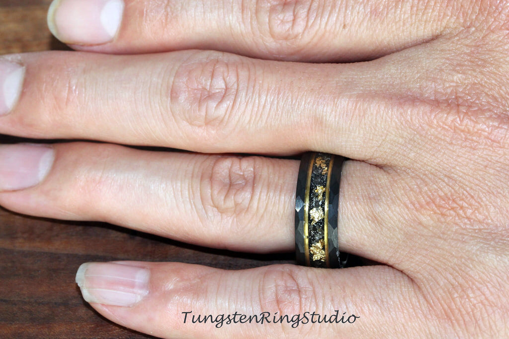 May include: A black tungsten ring with a gold inlay and a beveled edge. The ring is worn on a person's finger.
