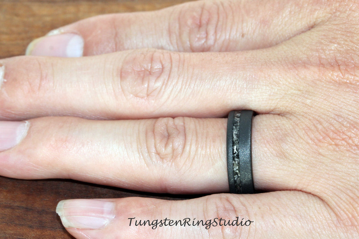 May include: A black tungsten carbide ring with a thin line of silver inlay. The ring is worn on a finger.