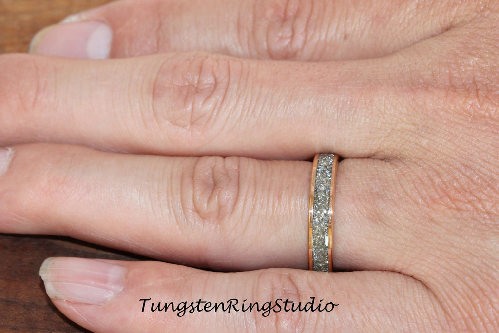 May include: A close-up of a silver tungsten ring with a rose gold band and a textured surface. The ring is worn on a person's finger.