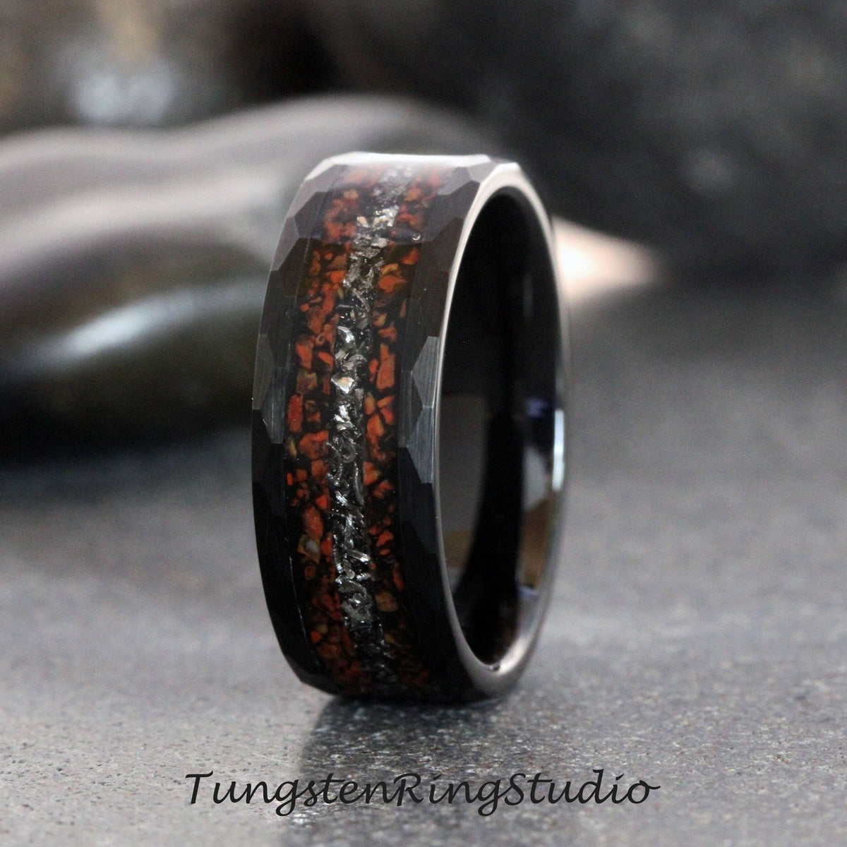 May include: A black tungsten carbide ring with a hammered finish and a red and silver inlay. The inlay is made of crushed stone and is set in a channel around the ring.