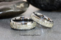 May include: Two silver tungsten carbide wedding bands with a light gray inlay. The inlay is made of crushed meteorite fragments.