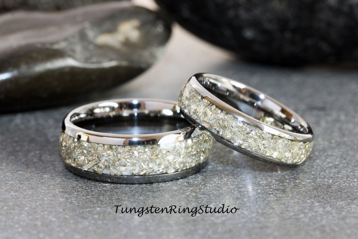 May include: Two silver tungsten carbide wedding bands with a light gray inlay. The inlay is made of crushed meteorite fragments.