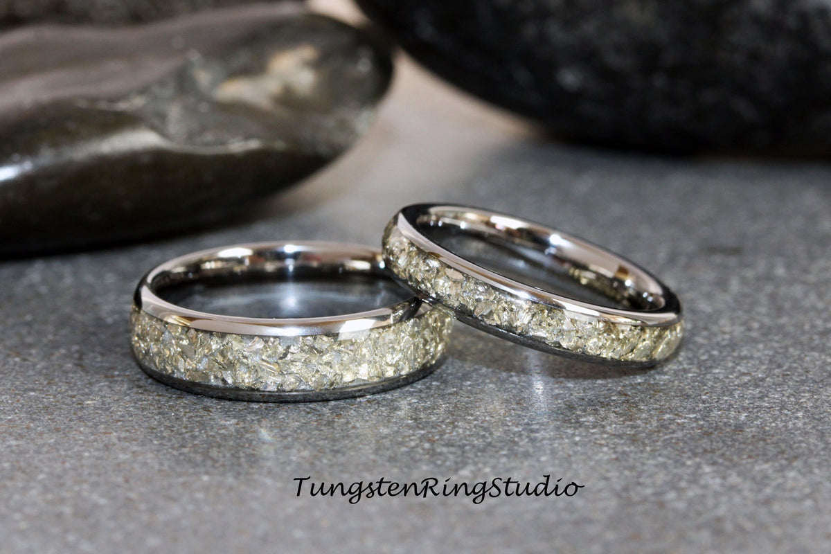 May include: Two silver tungsten carbide rings with a band of embedded light gray stones. The rings are on a gray surface.