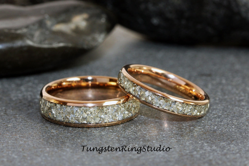 May include: Two rose gold tungsten carbide rings with a band of small, clear stones.