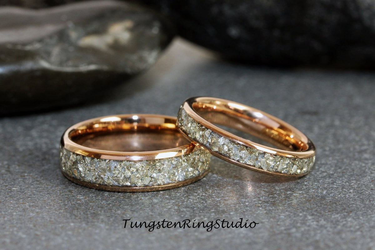 May include: Two rose gold tungsten carbide rings with a band of small, clear stones.