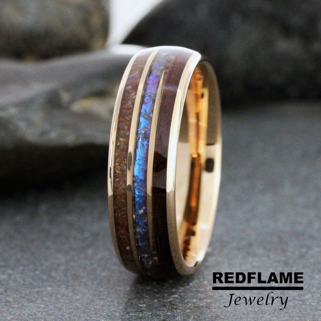 May include: A rose gold wedding band with a dark wood inlay and a blue and purple iridescent inlay. The band is made by Redflame Jewelry.