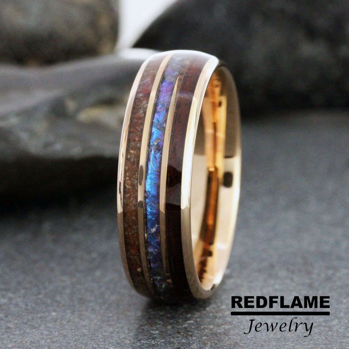 May include: A rose gold wedding band with a dark wood inlay and a blue and purple iridescent inlay. The band is made by Redflame Jewelry.