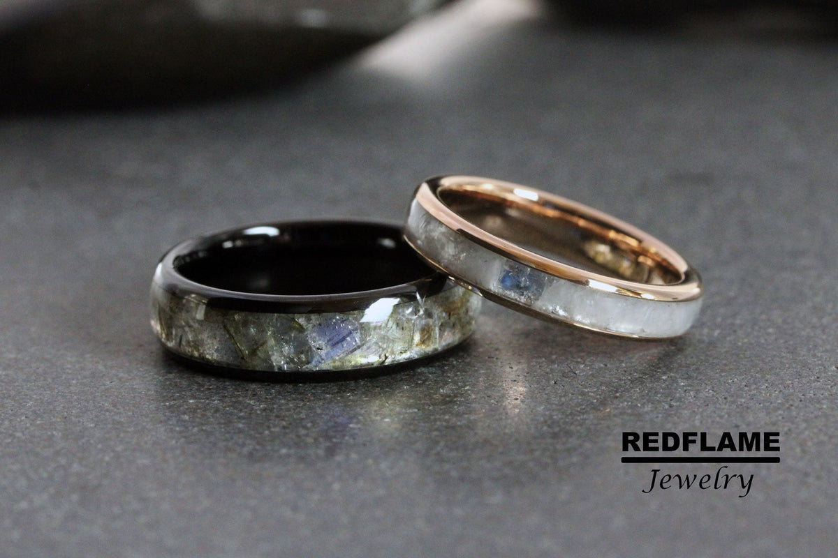 May include: Two wedding bands with a black and white metal band and a rose gold band. Both bands have a thin line of embedded gemstones.