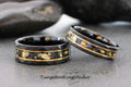 May include: Two black tungsten carbide rings with a gold inlay. The rings have a beveled edge and a textured surface. The gold inlay is made of real gold flakes.