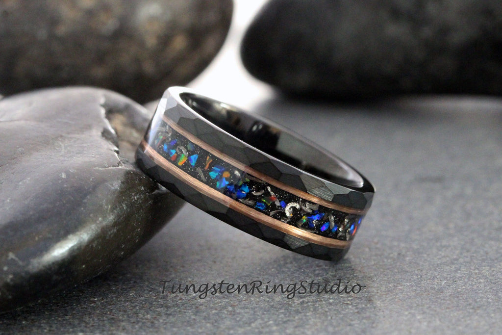 May include: Black tungsten ring with a hammered finish and a central inlay of opal and copper. The opal inlay features a mix of blue, green, and orange colors. The ring is a modern piece of jewelry.
