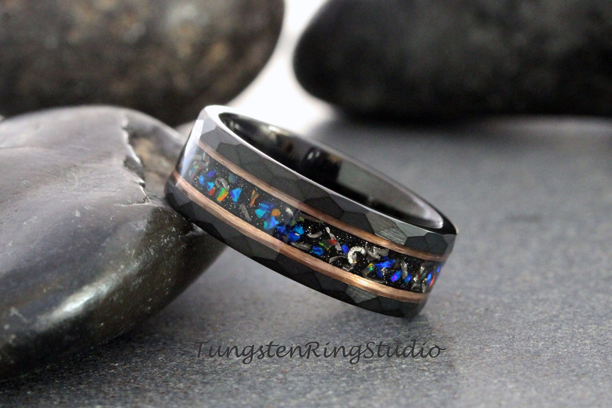 May include: Black tungsten ring with a hammered finish and a central inlay of opal and copper. The opal inlay features a mix of blue, green, and orange colors. The ring is a modern piece of jewelry.