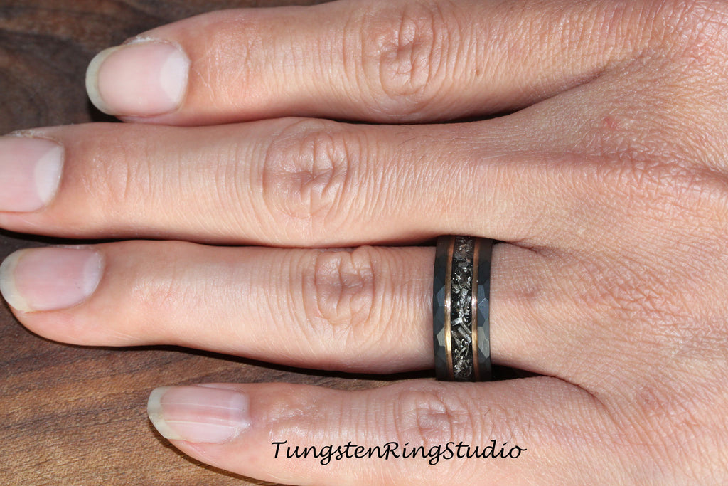 May include: A black tungsten carbide ring with a hammered finish and a thin rose gold band. The ring has a black and gold inlay design.