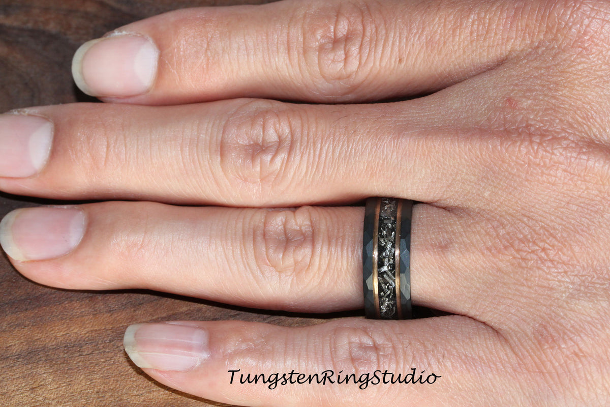 May include: A black tungsten carbide ring with a hammered finish and a thin rose gold band. The ring has a black and gold inlay design.
