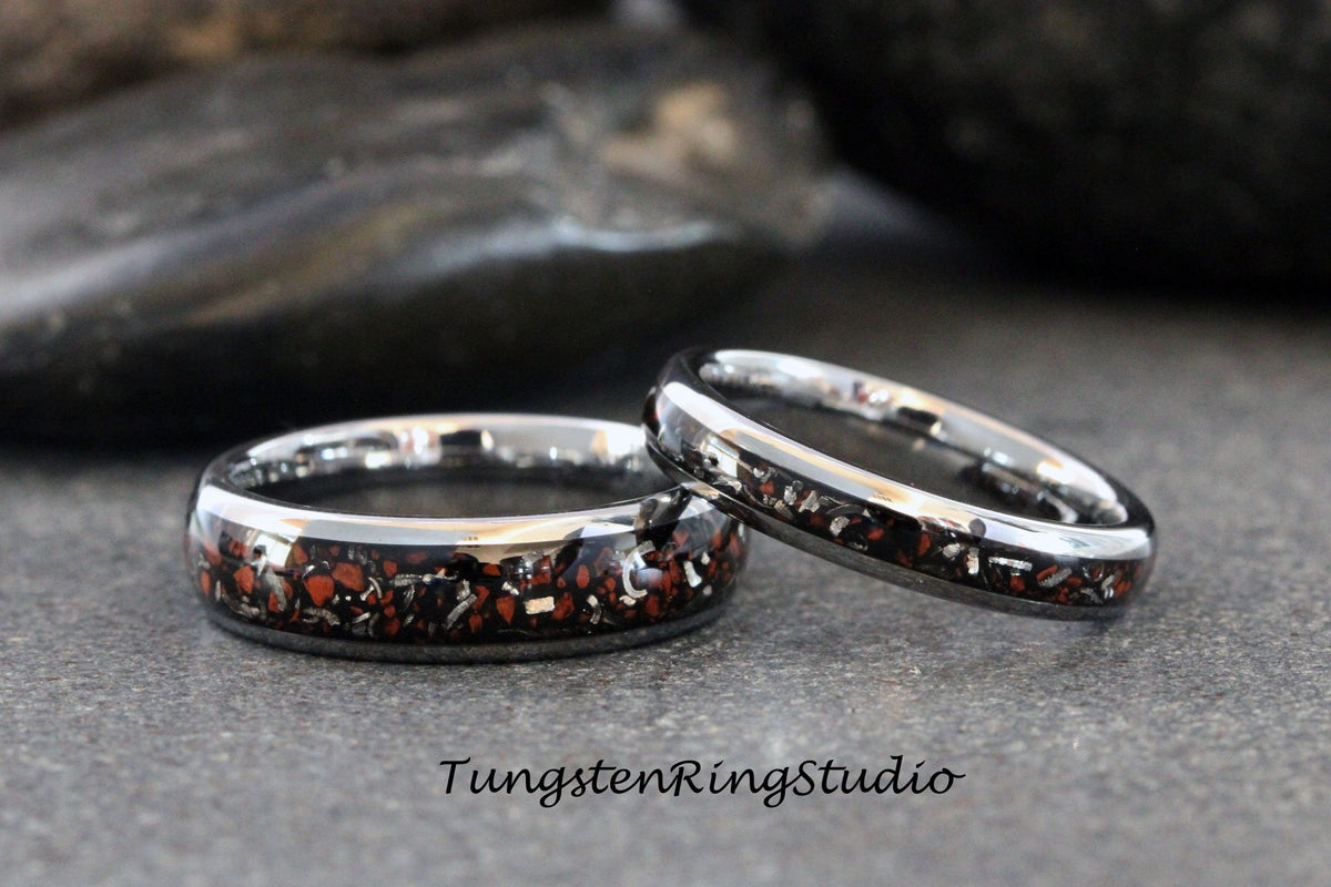May include: Two silver tungsten carbide rings with a black and red inlay. The rings are stacked on top of each other. TungstenRingStudio is printed below the rings.