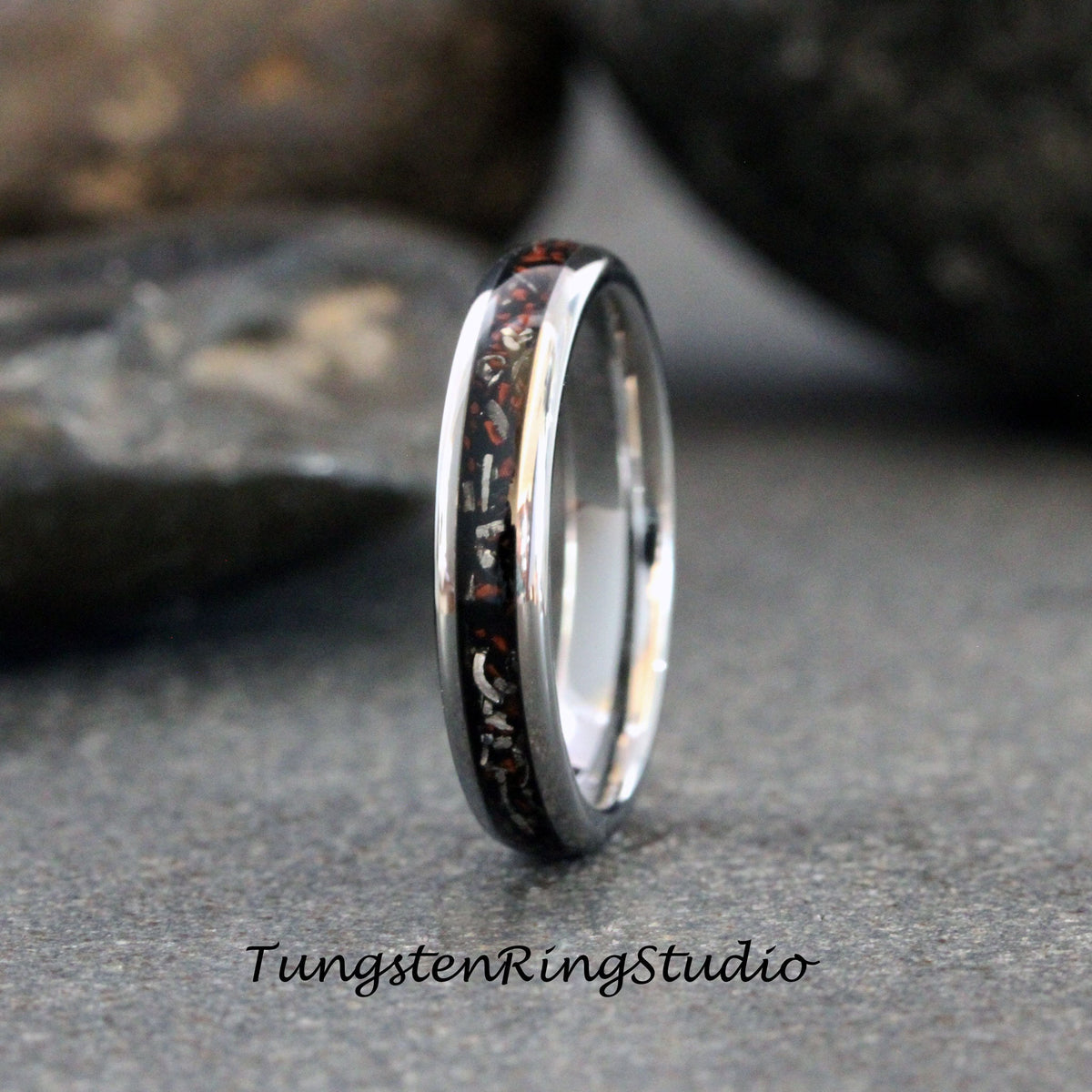 May include: A silver tungsten ring with a black and red inlay. The inlay is made of crushed meteorite and red jasper.