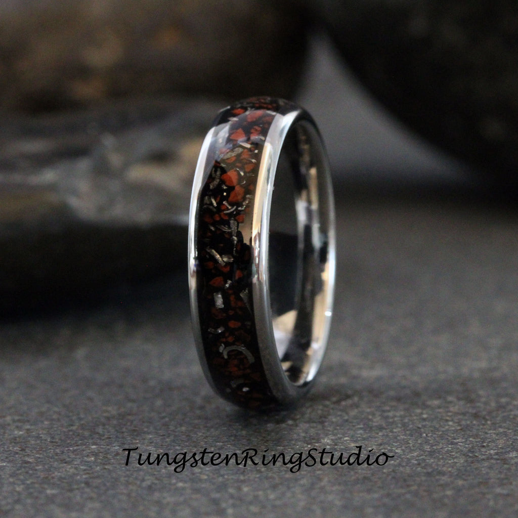 May include: A silver tungsten carbide ring with a black and red inlay. The inlay is made of meteorite fragments.