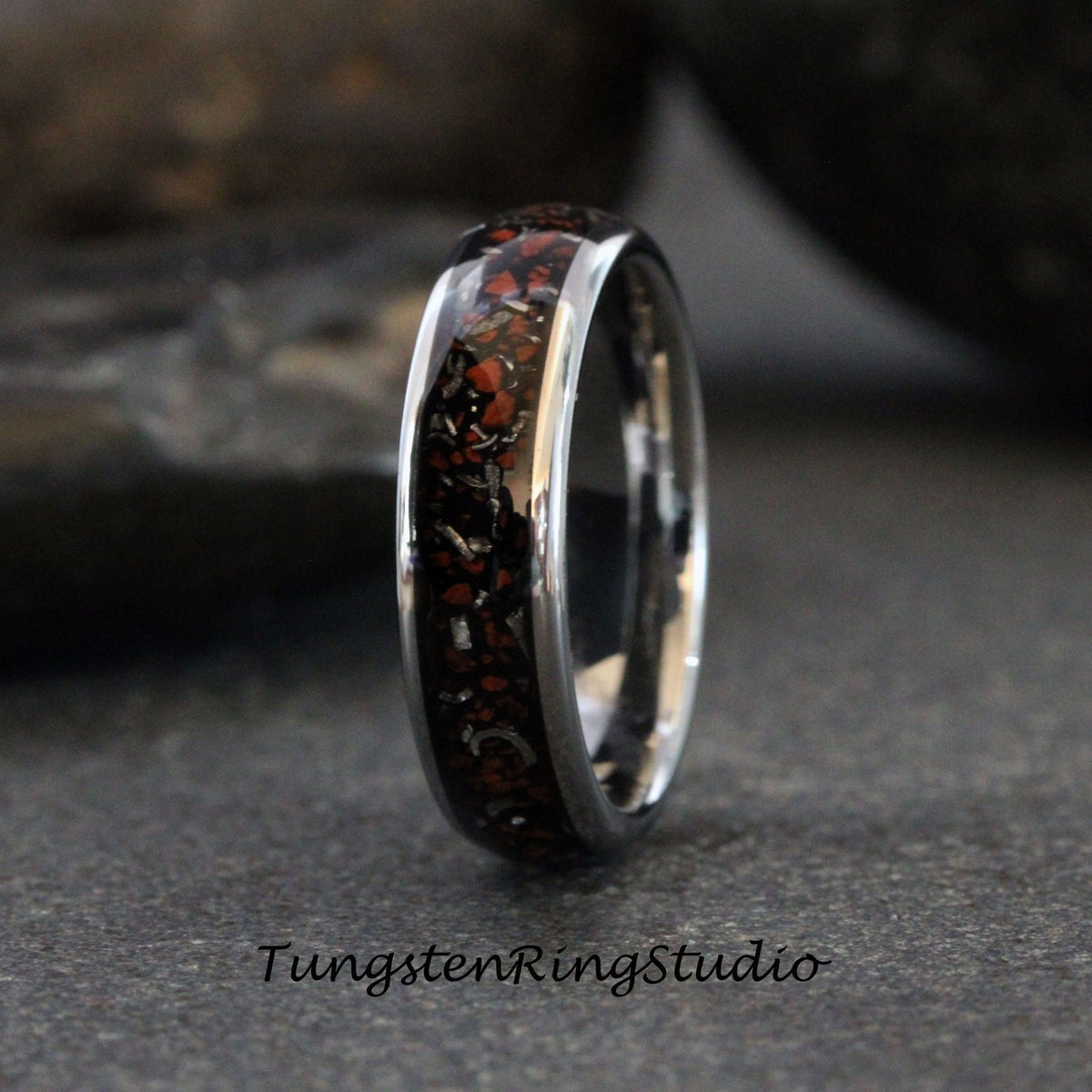 May include: A silver tungsten carbide ring with a black and red inlay. The inlay is made of meteorite fragments.