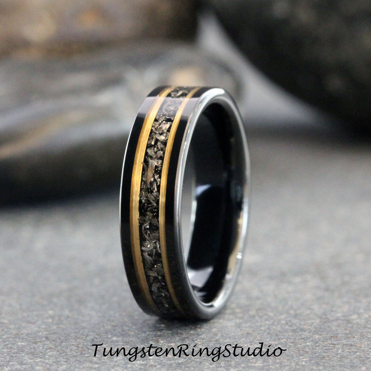 May include: A black tungsten carbide ring with a gold inlay and black meteorite particles. The ring is polished and has a beveled edge.