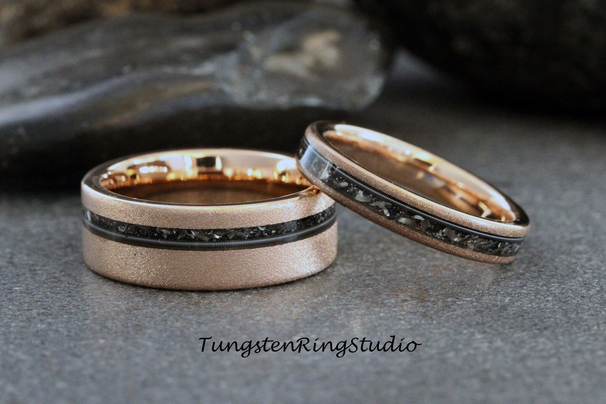 May include: Two rose gold tungsten carbide wedding bands with black inlay. The bands have a brushed finish and a thin black line around the edge.