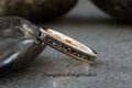 May include: A rose gold tungsten carbide ring with a black inlay. The inlay has a textured pattern.